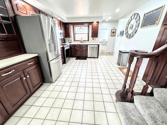 kitchen with appliances with stainless steel finishes, tasteful backsplash, sink, light tile patterned floors, and dark brown cabinets