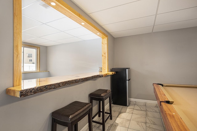 kitchen featuring stainless steel refrigerator, a paneled ceiling, and a kitchen breakfast bar