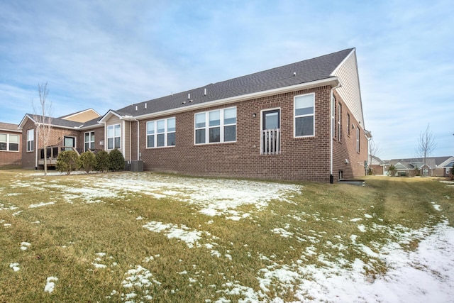 snow covered rear of property with cooling unit and a lawn