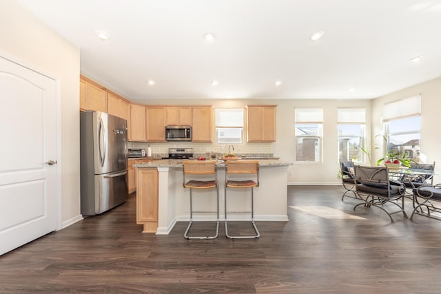 kitchen with light brown cabinets, light stone countertops, a center island, and appliances with stainless steel finishes