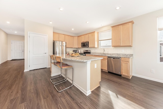 kitchen featuring a kitchen bar, light stone counters, tasteful backsplash, a center island, and stainless steel appliances