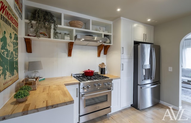 kitchen featuring arched walkways, butcher block countertops, extractor fan, stainless steel appliances, and open shelves