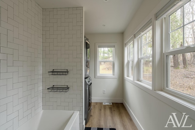 full bath featuring visible vents, shower / bathing tub combination, stacked washing maching and dryer, wood finished floors, and baseboards