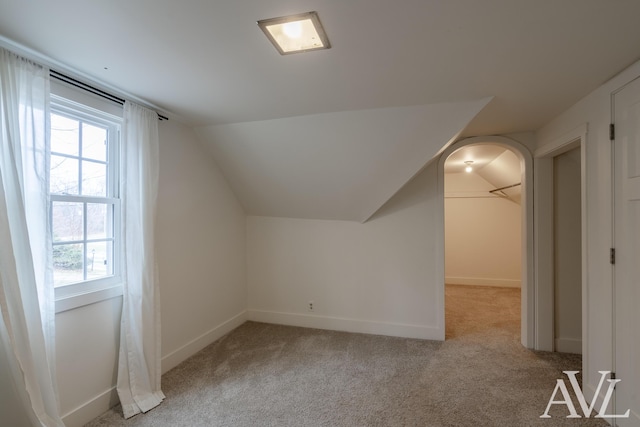 additional living space featuring baseboards, arched walkways, vaulted ceiling, and light colored carpet