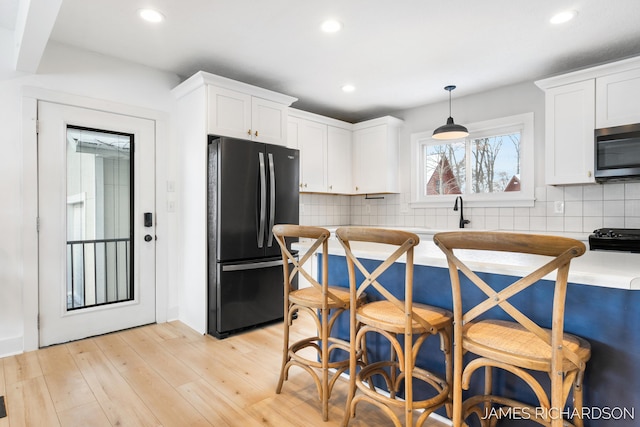 kitchen featuring white cabinets, freestanding refrigerator, decorative backsplash, light wood finished floors, and stainless steel microwave