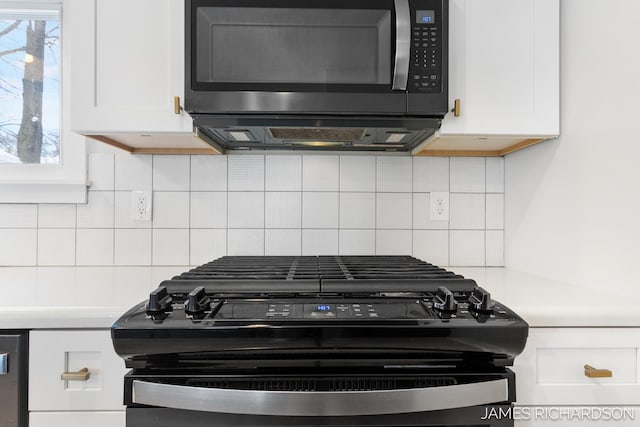 room details featuring tasteful backsplash, black range with gas stovetop, white cabinets, and stainless steel microwave