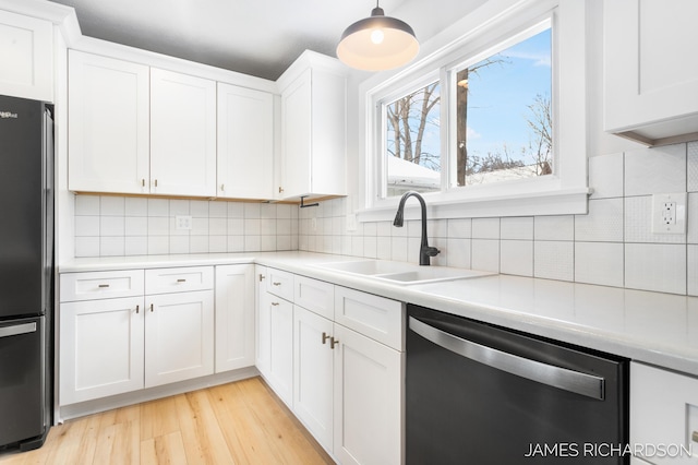 kitchen featuring light countertops, freestanding refrigerator, white cabinets, a sink, and dishwasher