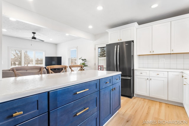 kitchen featuring light wood-style flooring, light countertops, blue cabinetry, backsplash, and freestanding refrigerator