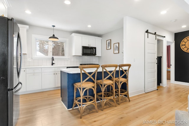 kitchen with backsplash, a barn door, freestanding refrigerator, light wood-type flooring, and a kitchen breakfast bar