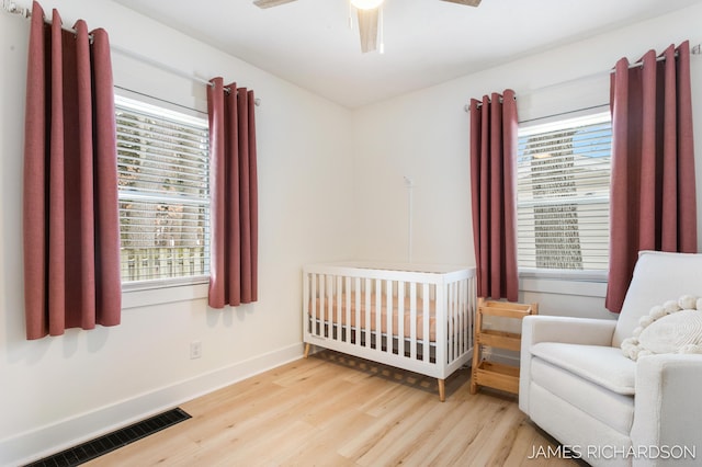 bedroom with wood finished floors, a ceiling fan, visible vents, baseboards, and a crib