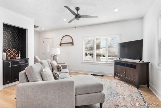 living room featuring light wood finished floors, baseboards, visible vents, and a ceiling fan