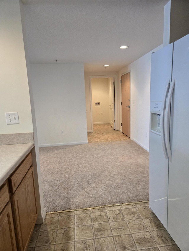 kitchen with white refrigerator with ice dispenser, light carpet, and a textured ceiling