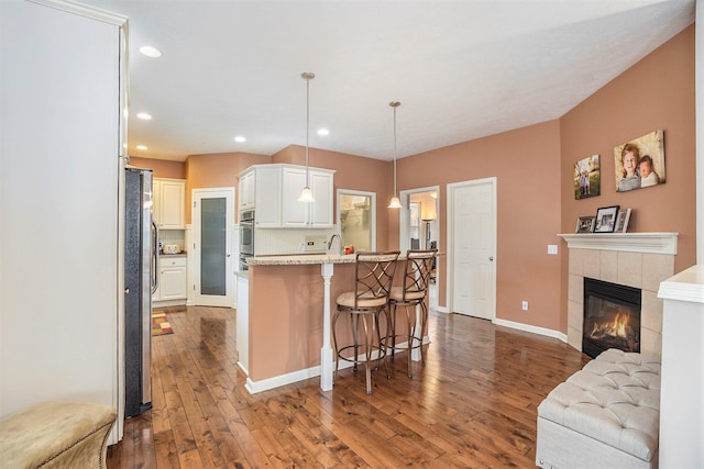 kitchen with dark wood-type flooring, a kitchen bar, decorative light fixtures, and white cabinets