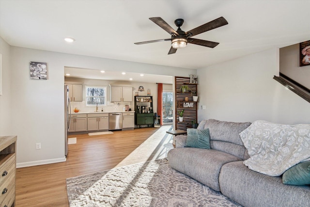 living room featuring ceiling fan, sink, and light wood-type flooring