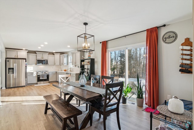 dining area featuring an inviting chandelier, sink, and light hardwood / wood-style floors