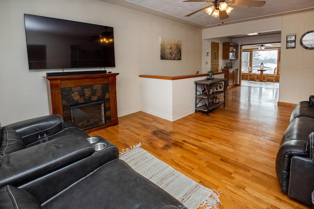 living room with ceiling fan, a stone fireplace, and light hardwood / wood-style flooring