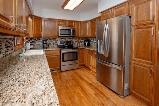 kitchen with sink, light hardwood / wood-style flooring, backsplash, stainless steel appliances, and light stone countertops