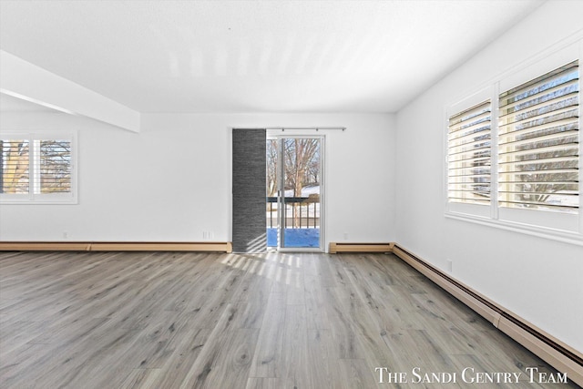 empty room featuring a healthy amount of sunlight, light hardwood / wood-style floors, and a baseboard heating unit