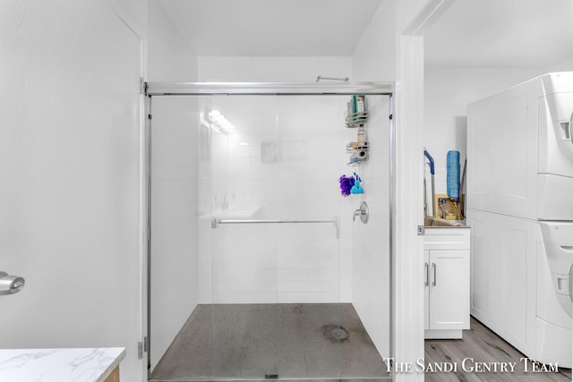 bathroom featuring wood-type flooring, stacked washer / drying machine, and an enclosed shower