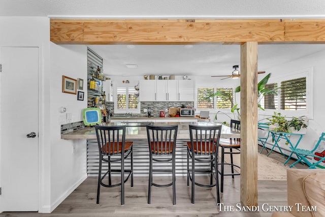 kitchen featuring a kitchen bar, tasteful backsplash, hardwood / wood-style flooring, ceiling fan, and white cabinets