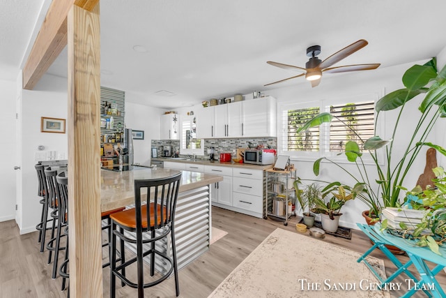 kitchen with ceiling fan, white cabinets, light hardwood / wood-style floors, and decorative backsplash