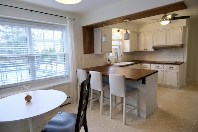 kitchen featuring butcher block counters, sink, a breakfast bar area, white cabinetry, and kitchen peninsula