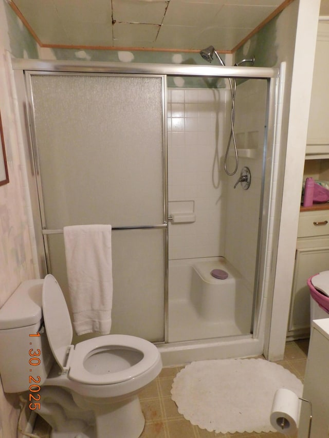 bathroom featuring toilet, an enclosed shower, and tile patterned flooring