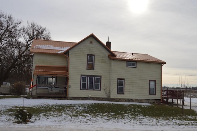 snow covered rear of property featuring metal roof, a porch, and a chimney