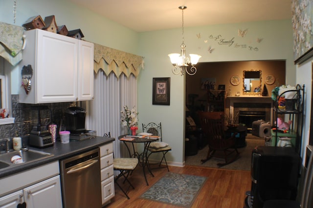 kitchen with dark wood finished floors, dark countertops, stainless steel dishwasher, a fireplace, and a sink