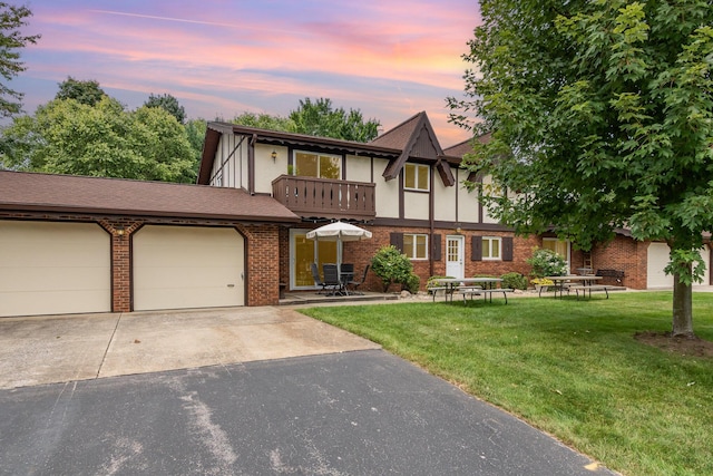 tudor-style house with a garage, a lawn, and a balcony