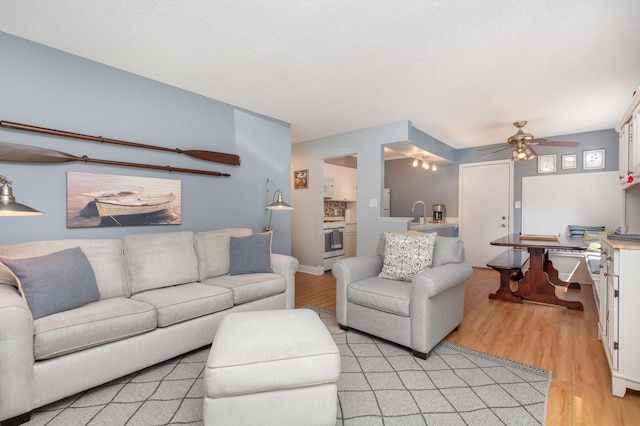 living room featuring ceiling fan, light hardwood / wood-style flooring, and a textured ceiling