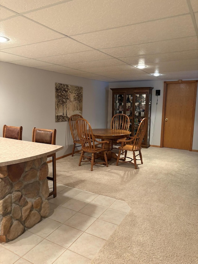 dining space with a drop ceiling and light colored carpet