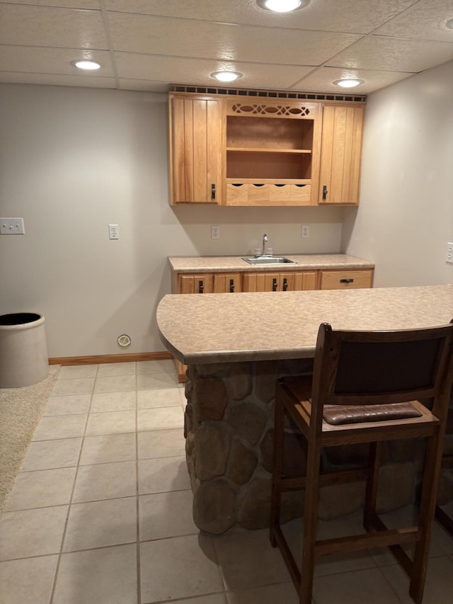 bar featuring a paneled ceiling, light brown cabinetry, and sink