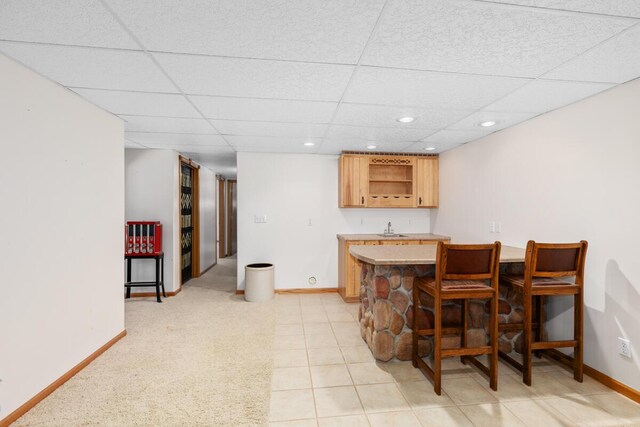 kitchen with light brown cabinetry, sink, a paneled ceiling, and a breakfast bar area