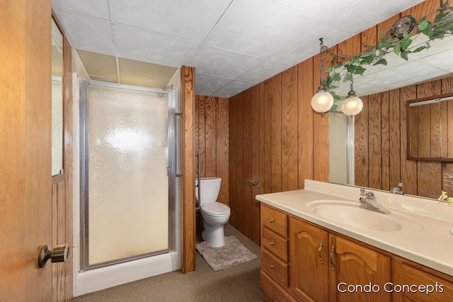 bathroom with vanity, a shower with shower door, toilet, and wood walls