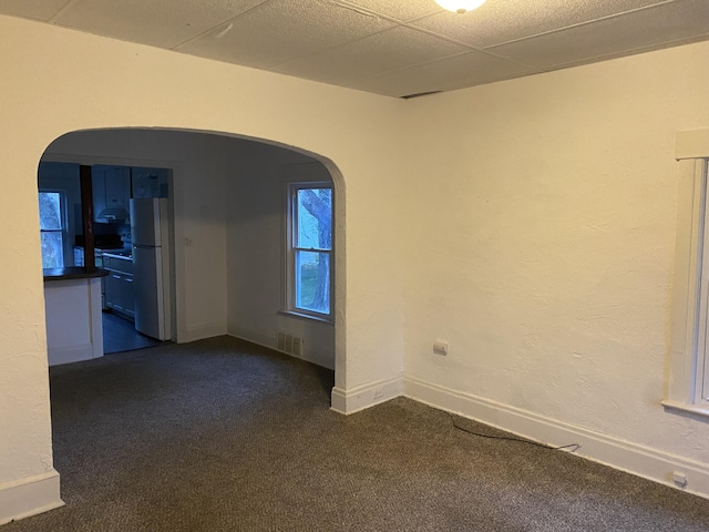 empty room featuring a paneled ceiling and dark colored carpet