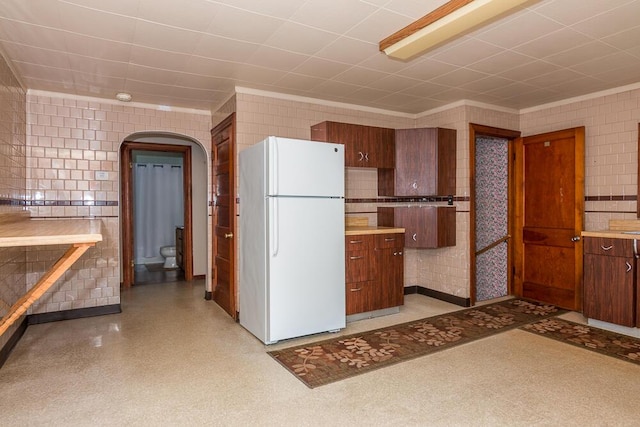 kitchen featuring white refrigerator, ornamental molding, and tile walls