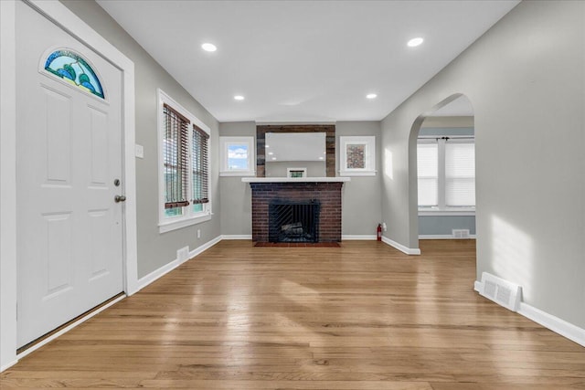 unfurnished living room featuring a brick fireplace, a healthy amount of sunlight, and light wood-type flooring