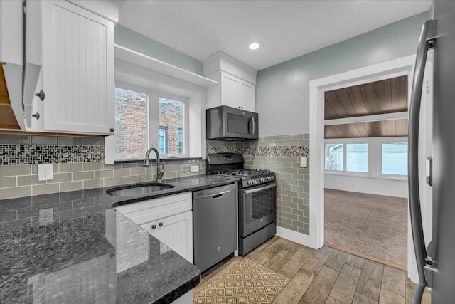 kitchen with appliances with stainless steel finishes, white cabinetry, sink, dark stone counters, and light wood-type flooring