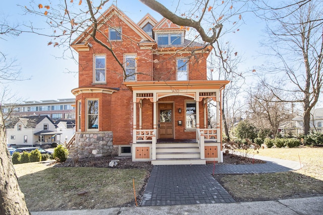 view of front facade with brick siding, covered porch, an attached garage, and decorative driveway