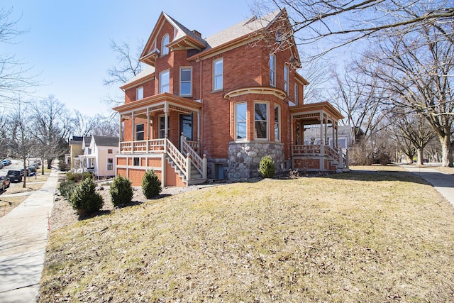 victorian home with a chimney, brick siding, a porch, and a front lawn