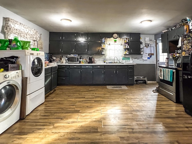 kitchen with appliances with stainless steel finishes, sink, washing machine and clothes dryer, and light hardwood / wood-style flooring