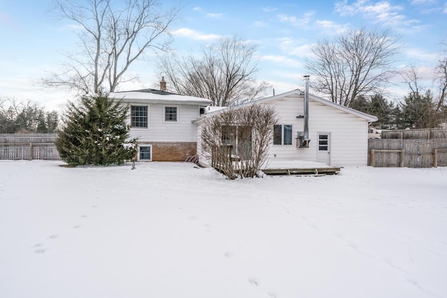 snow covered rear of property featuring fence, a chimney, and a wooden deck