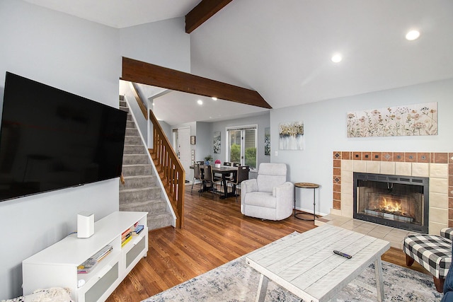 living room featuring a tiled fireplace, vaulted ceiling with beams, and hardwood / wood-style floors