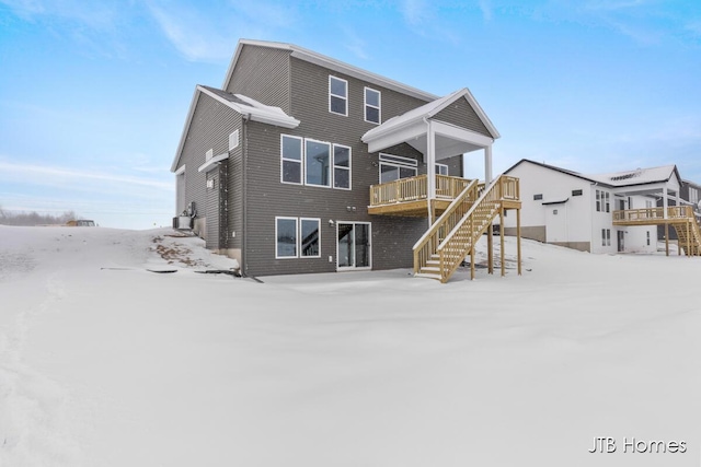 snow covered house featuring stairway and a wooden deck