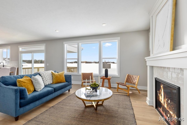 living room with a glass covered fireplace, light wood-style flooring, and baseboards