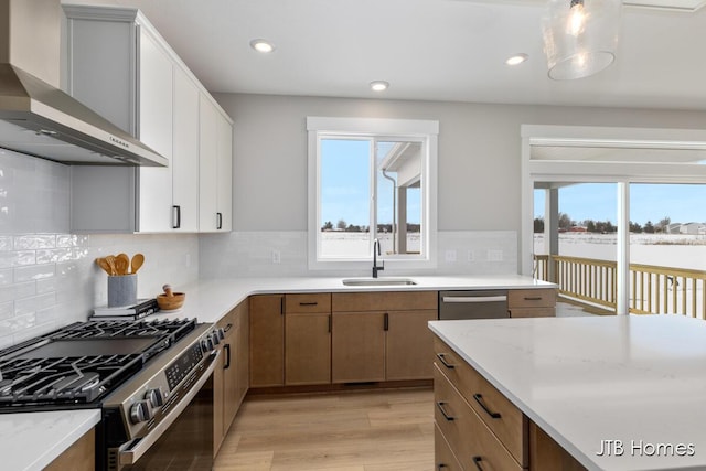 kitchen featuring brown cabinets, wall chimney range hood, stainless steel appliances, and a sink