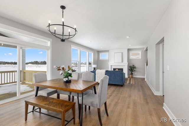 dining space featuring a warm lit fireplace, a notable chandelier, baseboards, and light wood-style floors