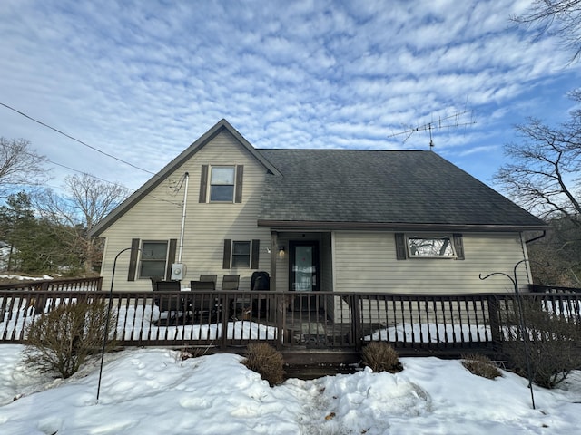 snow covered back of property with a deck and a shingled roof