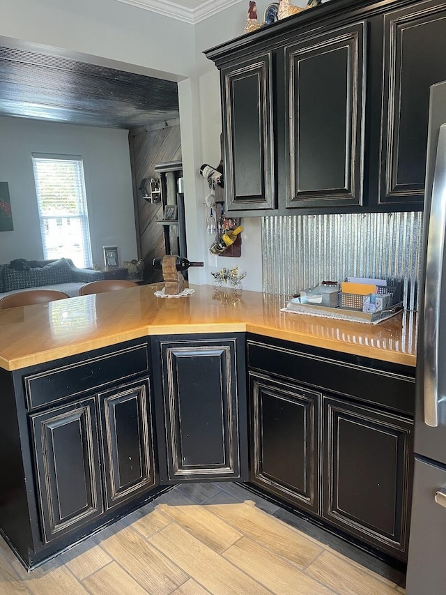 kitchen with crown molding, kitchen peninsula, stainless steel refrigerator, and light wood-type flooring